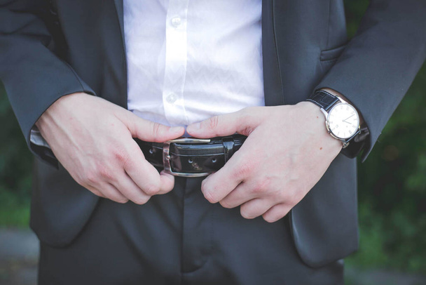 A closeup shot of a groom fixing his belt - 写真・画像