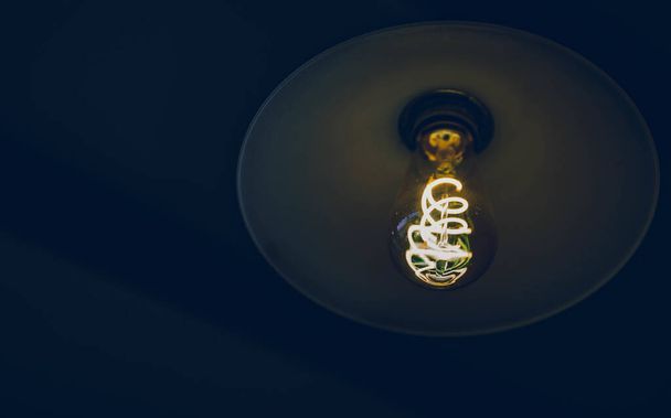 A low angle shot of an old-style vintage glowing light bulb in a dark setting - Foto, afbeelding