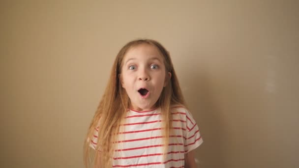 Portrait of happy small blonde girl looking into camera and raises hands rejoicing achievement indoor. Little funny female child with positive emotions on her face inside. Close up Slow motion - Footage, Video