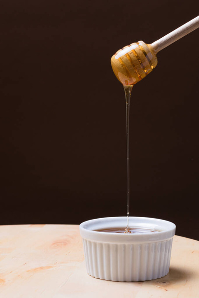 A vertical shot of a honey dipper flowing into a bowl - Φωτογραφία, εικόνα