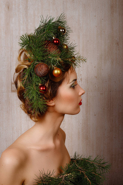 Beautiful happy young lady with a Christmas pine wreath on her head and fashione xmas tree dress, decorated with Christmas balls, berries and snowflakes. New Year Concept - Foto, imagen