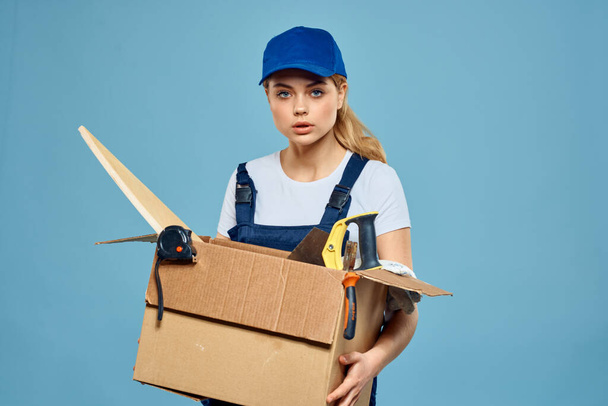 Робоча жінка в уніформі з коробкою в руках інструменти завантаження служби доставки синій фон
 - Фото, зображення