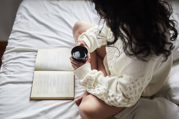 Una joven latina tomando café y leyendo un libro en la cama - Foto, Imagen