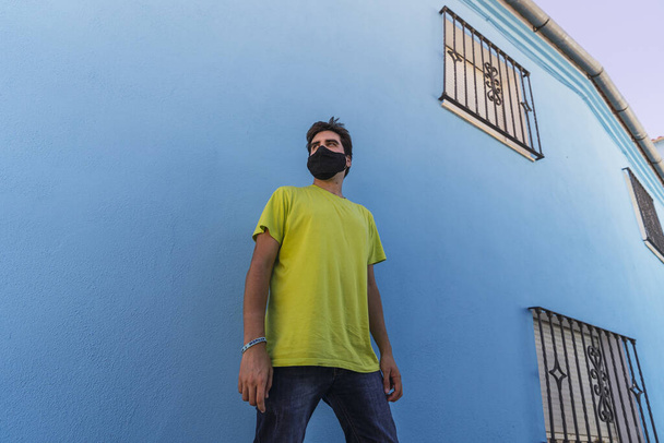 A low angle shot of a male wearing a mask while standing by a blue wall - 写真・画像