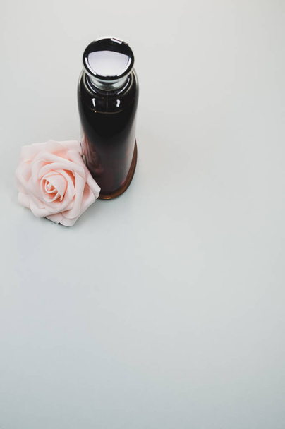 Une bouteille de parfum rose et une rose sur fond gris - Photo, image