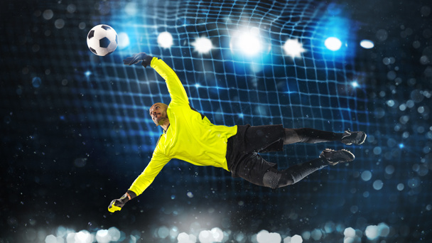 Portiere di calcio, in uniforme fluorescente, che fa un grande salvataggio ed evita un gol su fondo blu scuro - Foto, immagini