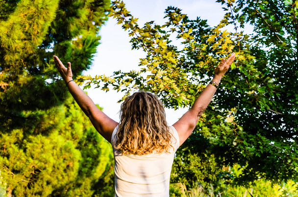 A female standing with her hands raised to the sky in a park - feeling free concept - Φωτογραφία, εικόνα