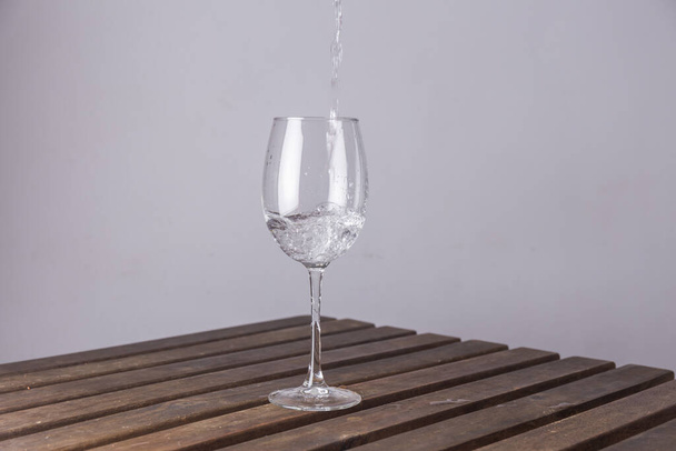 A crystal goblet on a wooden table filling with water on white background - Photo, Image