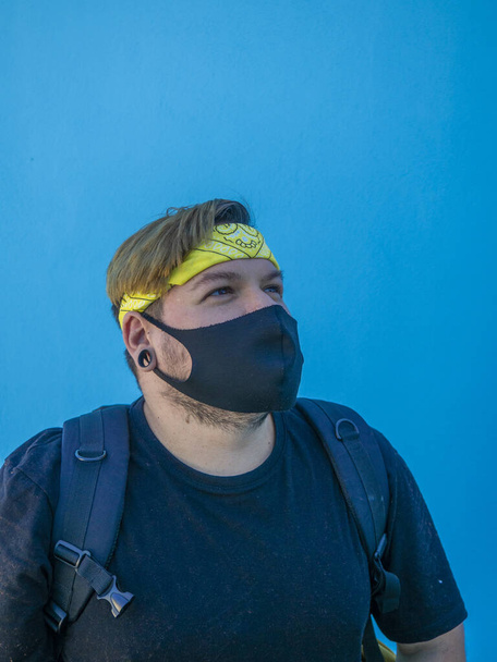A young Caucasian male with a medical mask standing against a blue wall in Andalusia, Spain - the new normal after Covid-19 - Foto, Bild