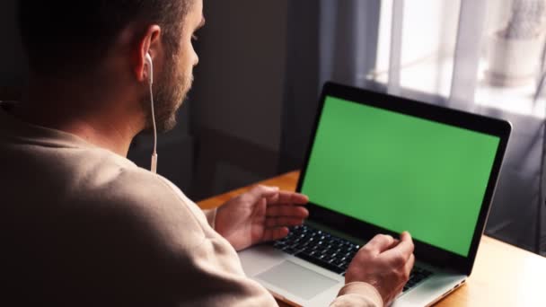 Молодий чоловік у домашньому офісі сидить за столом і розмовляє з комп'ютером з зеленого ноутбука. Чоловік розмовляє через інтернет-дзвінок з веб-камери - Кадри, відео