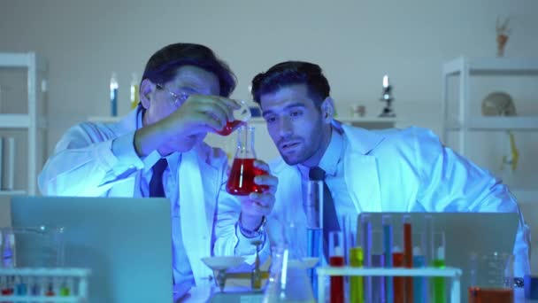 En un laboratorio de ciencias por la noche, dos científicos estaban vertiendo material en un tubo de ensayo y registrando los resultados. Trabajan apresuradamente para obtener los resultados rápidamente. - Imágenes, Vídeo