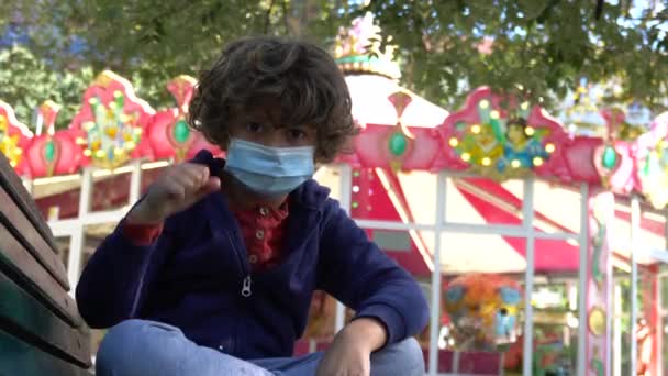 Kleine jongen met trieste stemming op de speelplaats dragen gezichtsmasker buiten tijdens covid - Video