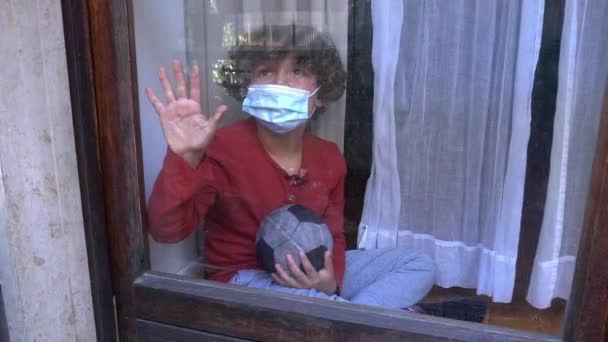 blanco caucásico niño 6 años en cuarentena casa con máscara mira por la ventana de la casa durante el bloqueo del Coronavirus en Europa, América y Asia - Imágenes, Vídeo