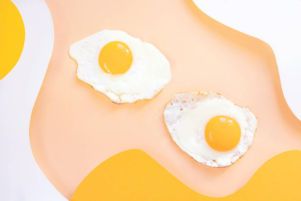 Τηγανητά αυγά σε ανοιχτό λευκό και κίτρινο κυματιστό φόντο. Χάρτινη τέχνη Πρωινό, τηγανιτό φαγητό. - Φωτογραφία, εικόνα