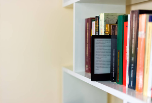 Un e-book mezzo posto su uno scaffale pieno di libri tradizionali come se fosse un altro - Foto, immagini