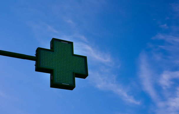 Desde un ángulo bajo se puede ver una cruz de farmacia verde en un cielo azul con algunas nubes claras - Foto, imagen