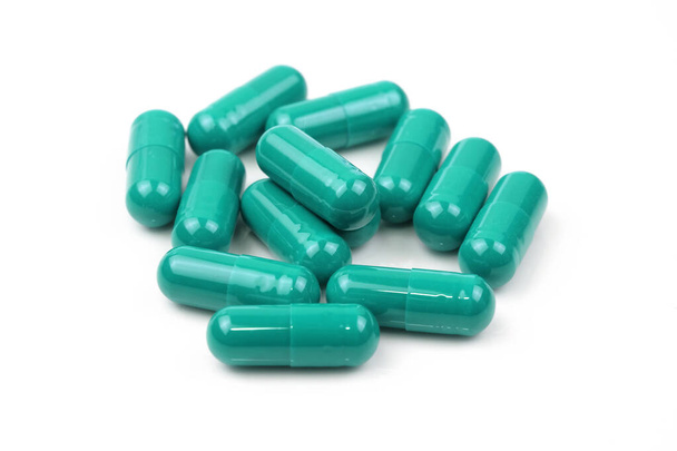 Groene capsules op een witte achtergrond. Groene tabletten in een shell close-up. Levensmiddelenadditieven, medicijnen, kalmeringsmiddelen. - Foto, afbeelding