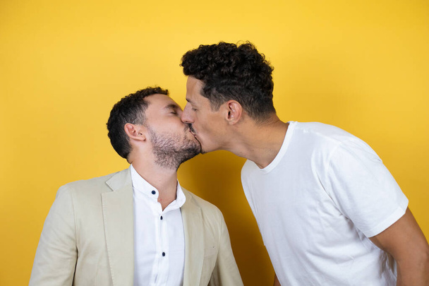 Jeune couple gay de deux hommes portant des vêtements décontractés sur fond jaune isolé Debout avec sourire sur le visage embrassant sur fond blanc isolé - Photo, image