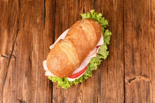 Sappige rosbief sandwich met gekookte worst, salade en tomaten op de houten tafel, top viwe. - Foto, afbeelding