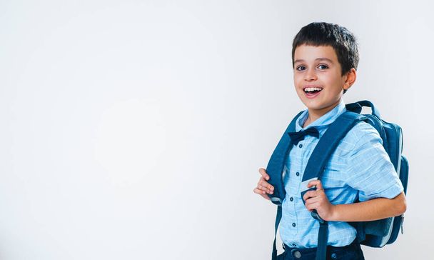 The schoolboy in a shirt with a bow tie and a backpack behind his back stands half a turn and laughs. Conceptual. Copy space. - Fotoğraf, Görsel