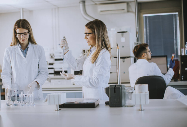Χαριτωμένες γυναίκες ερευνητές με λευκή ρόμπα εργαστηρίου που εργάζονται στο εργαστήριο - Φωτογραφία, εικόνα