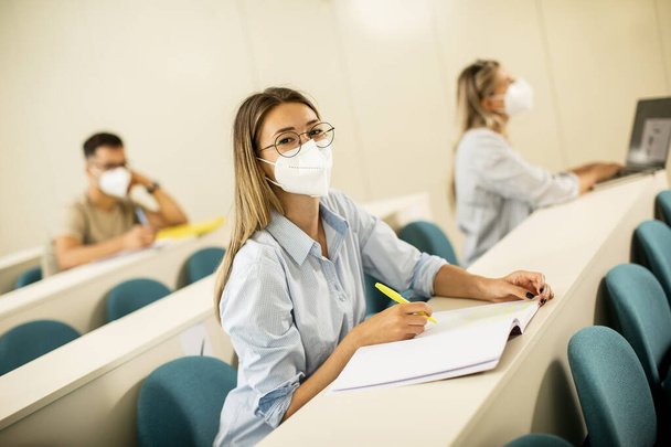 Mladá studentka nosí ochrannou masku obličeje pro ochranu proti virům v přednáškovém sále - Fotografie, Obrázek