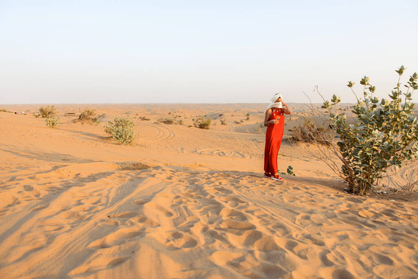 Girl in a bright dress and a turban in the sands of the emirate at sunset - Foto, Imagem