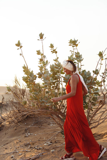 Girl in a bright dress and a turban in the sands of the emirate at sunset - 写真・画像