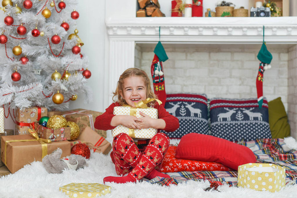 Beautiful little girl holding a gift, in the bright New Year's interior - Foto, Bild