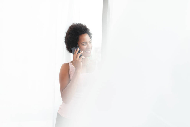 Heureuse femme afro-américaine parlant sur un téléphone portable près de la fenêtre - Photo, image