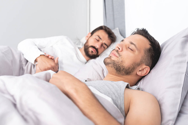 Young gay couple sleeping on bed with hands clasped at home - Foto, Imagem