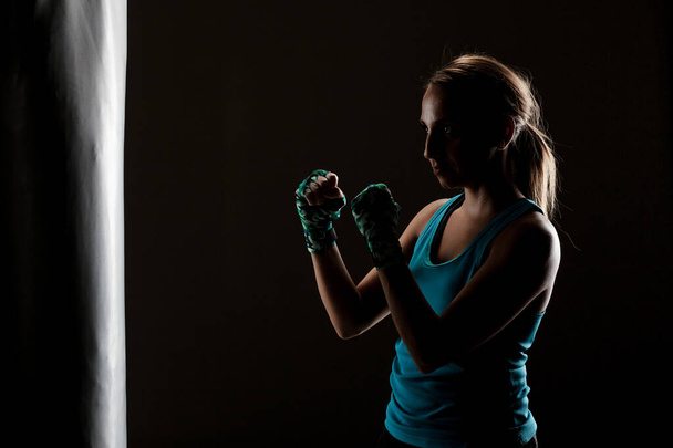kick fighter girl in front of a boxing bag - Foto, Bild
