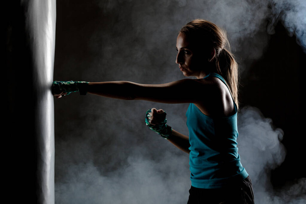 kick fighter girl punching a boxing bag. smoke in the air - Valokuva, kuva