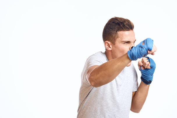 urheilullinen mies nyrkkeilijä sinisissä käsineissä harjoitellen lyöntejä kevyellä taustalla rajatulla näkymällä - Valokuva, kuva