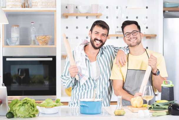Two happy male friends holding rolling pins cooking food in modern domestic kitchen - Фото, зображення