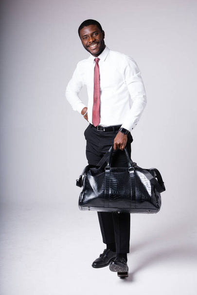 dark-skinned man holding a black backpack and a black leather bag. Stands on a white background - Fotoğraf, Görsel