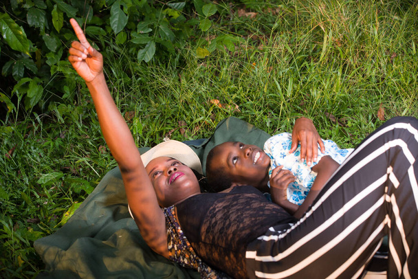 young woman lying in hat in a park showing something to her child smiling. - Photo, Image