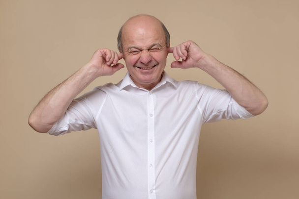 Senior Kaukasische man bedekt zijn oren proberen te voorkomen dat horen spoilers. - Foto, afbeelding