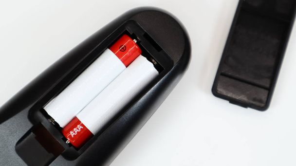 Schwarze TV-Fernbedienung mit AAA-Alkaline-Batterien in rot und weiß auf weißem Hintergrund. Batteriewechsel, Ersatzteile. Fernbedienung Batteriefach in Nahaufnahme - Foto, Bild