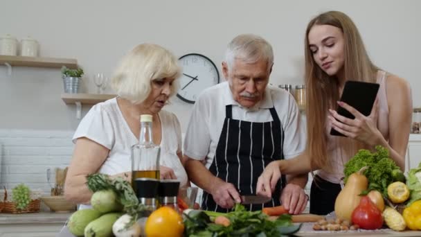 Vanhempi isovanhemmat pari leikkaamalla vihanneksia salaattia, kuuntelu resepti tyttö tabletti - Materiaali, video