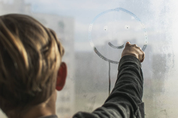 A little boy draws a smiley face on a fogged, wet window - Foto, Bild