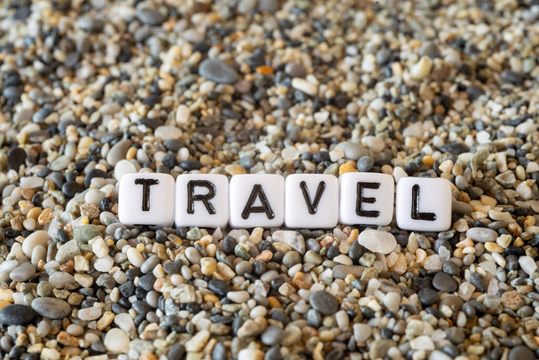 Texto de la inscripción de viaje con el nombre de la ciudad de destino de vacaciones en una naturaleza muerta de las letras dispuestas en una arena de la orilla piedras - Foto, imagen