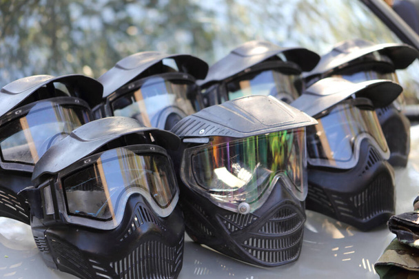 Protective paintball black masks on the hood of a car in a row, on a sunny day outdoors. Black protective gotcha mask. - Fotó, kép