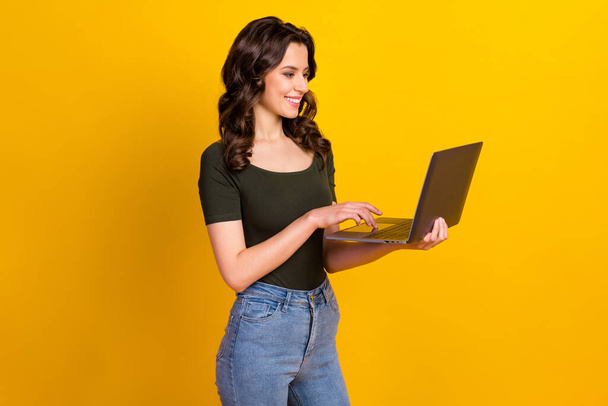 Profile side view portrait of her she nice attractive lovely cheerful cheery smart clever wavy-haired girl holding in hand laptop working isolated on bright vivid shine vibrant yellow color background - Fotó, kép