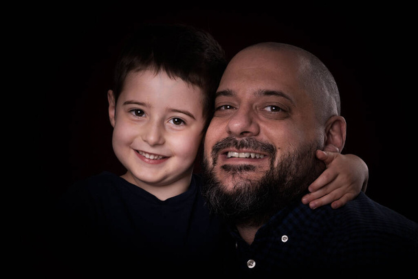 Portrait bearded father and son smile for camera on black background - Fotoğraf, Görsel
