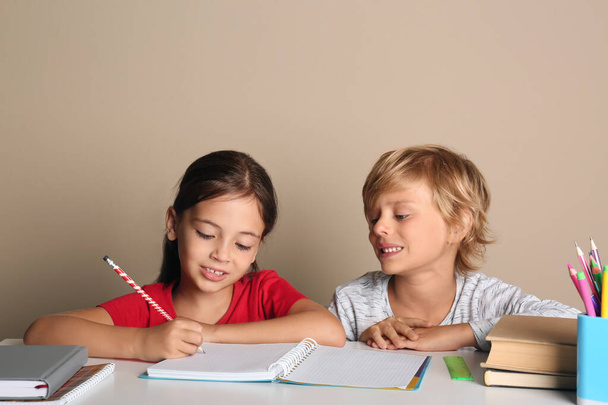 Little boy and girl doing homework at table on beige background - Fotó, kép