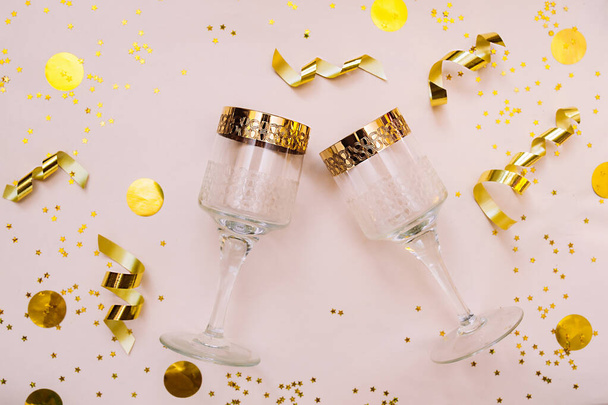Duas bebidas copos feitos de vidro com uma borda de ouro sobre fundo rosa com decorações de ouro, lantejoulas, estrelas, fitas de papel alumínio e um grande arco de ouro para embalagem. Um layout festivo para o conteúdo - Foto, Imagem