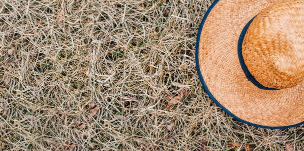žlutý proutěný klobouk se širokým okrajem a modrou páskou na suché trávě v létě. Nápis - Fotografie, Obrázek