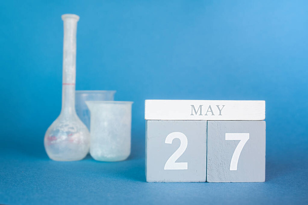 日付とカレンダーの木製のキューブは、青色の背景に27と化学試験管があります。化学者の日のためのポストカード. - 写真・画像