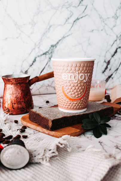 Ωραίο κάθετο πρωινό σε καραντίνα. καφέ χάρτινο Κύπελλο με την επιγραφή Απολαύστε σε ένα μαρμάρινο τραπέζι με μια τουρκική καφετιέρα, διάσπαρτους κόκκους καφέ και φράουλες - Φωτογραφία, εικόνα